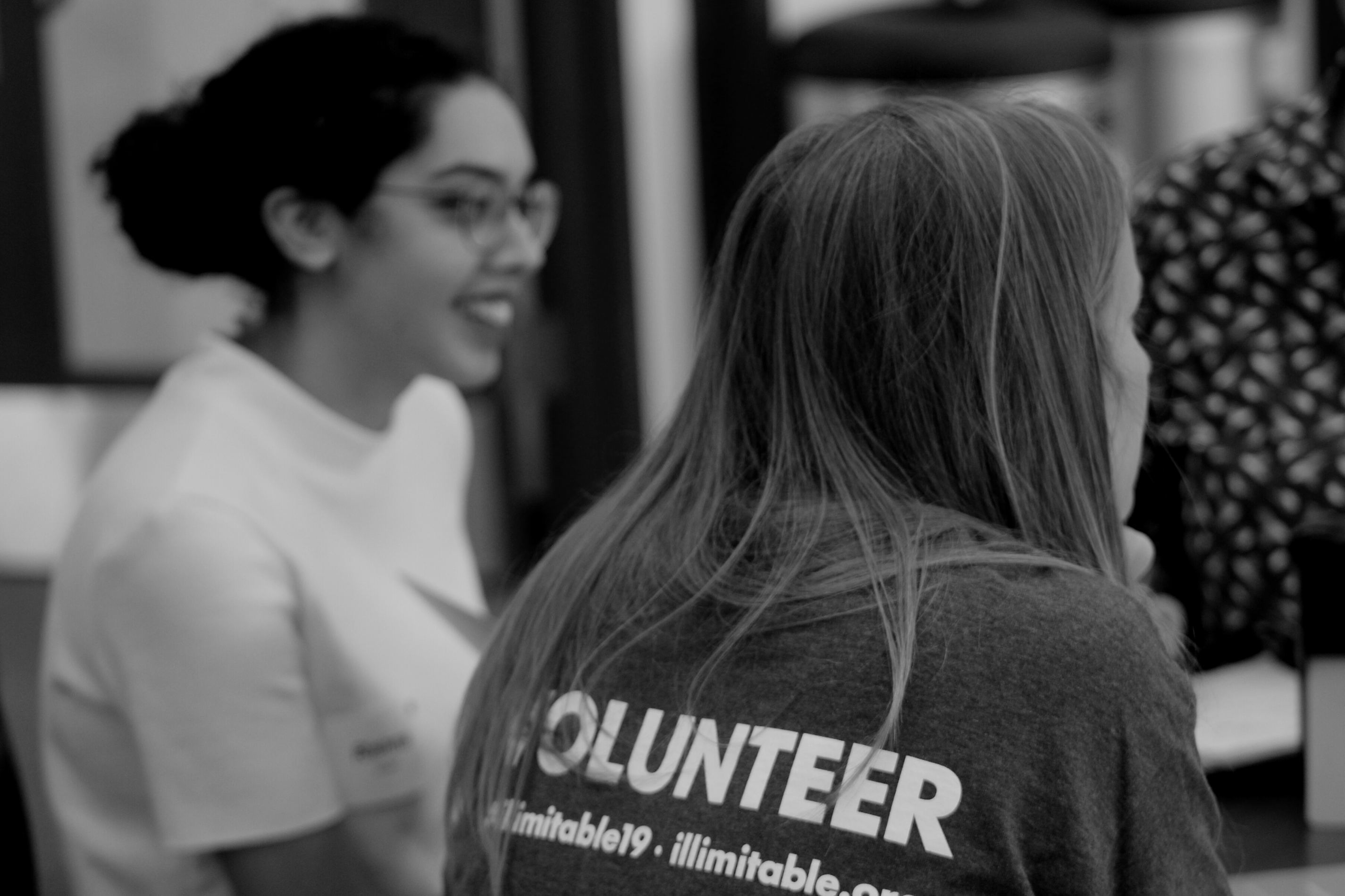 In focus is an Illimitable volunteer mentoring a design team and in the background is a team member smiling.