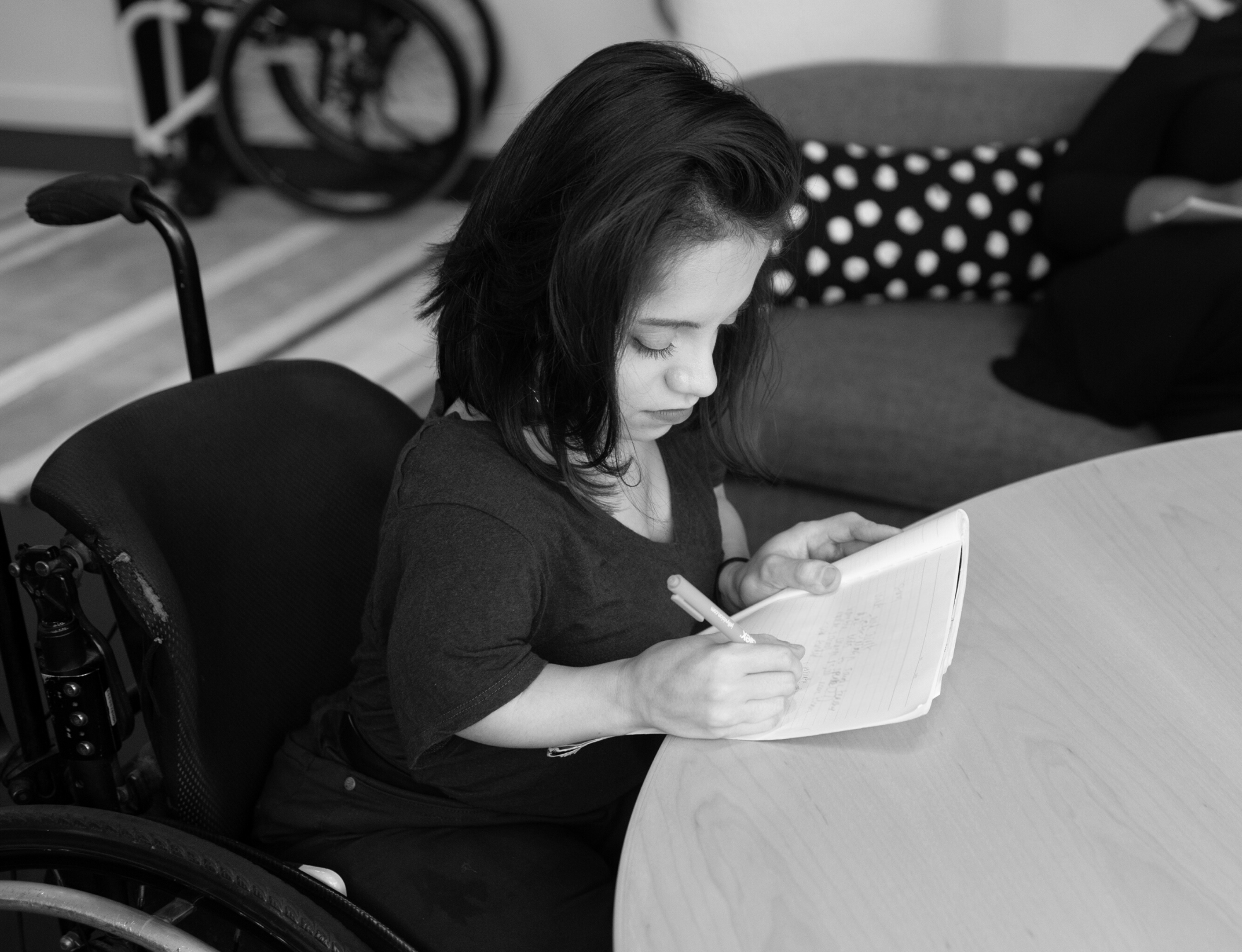 A South Asian woman in her wheelchair takes notes by hand during a meeting.